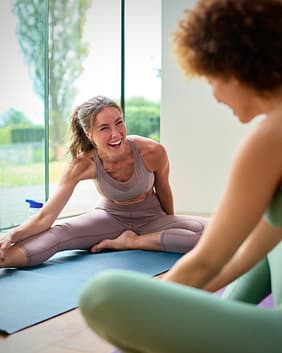 Two Female Friends Wearing Fitness Clothing Stretching In Gym Or Yoga Class